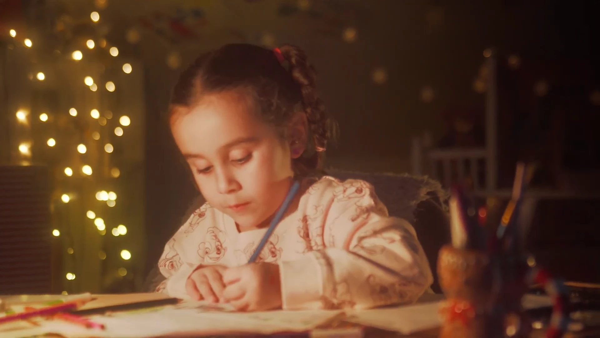 Niña dibujando en su mesa, con luces de navidad de fondo